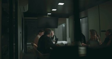 Toplantı sırasında toplantı masası etrafında çeşitli iş adamları, modern ofis konferans odasında dizüstü bilgisayar ve tabletler kullanarak ciddi tartışmalara giriyorlar.