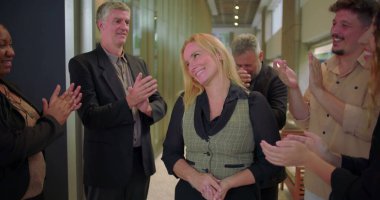 Ofis koridorundaki çeşitli iş arkadaşlarından alkış alan gülümseyen kadın, başarıyı kutlayan ve iş yerinde takdir gösteren bir grup profesyonel.