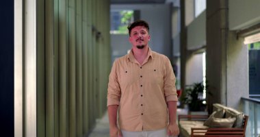 Ofis koridorunda yumruklarını sıkmış ve kararlı bir ifadeyle duran adam arka planda oturma alanı olan modern koridorda poz verdi.