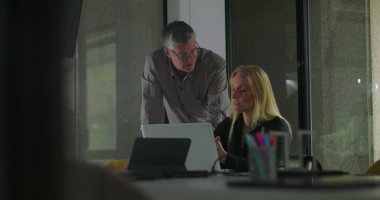 Erkek iş arkadaşı ekranı işaret ederken, sarışın iş kadını ofis toplantı odasında iş birliği yaparken dinliyor ve ilişki kuruyor.