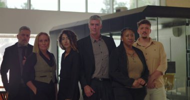 Modern ofiste, ciddi ifadeler takınan altı profesyonelden oluşan çeşitli bir grup. Parlak şirket ortamında grup portresi yapmak için birlikte poz verdiler. 