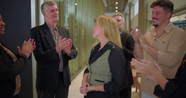 Ofis koridorundaki çeşitli iş arkadaşlarından alkış alan gülümseyen kadın, başarıyı kutlayan ve iş yerinde takdir gösteren bir grup profesyonel.