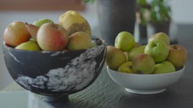 Taze elma ve armutla dolu iki kase mutfak tezgahında oturup doğal rengi, dokuyu ve sakin bir ev ortamını vurgulayan basit bir hayat sahnesi oluşturuyor.