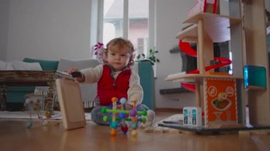 Bebek çeşitli oyuncakların arasında oturur ve parlak bir faaliyet parçasına dokunmak için öne doğru eğilir, rahat oyun sırasında sürekli bir bağlılık ve doğal merak gösterir.