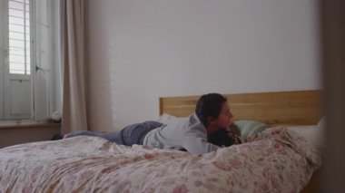 Bir anne yatakta yatarken, yeni yürümeye başlayan çocuğu birlikte basit, rahat bir sabah geçirir. Bu da günlük aile hayatını, rahatlığı ve yakınlığı yansıtır.