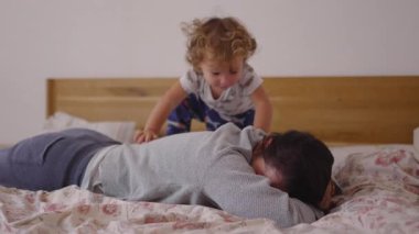 Yeni yürümeye başlayan bir çocuk annesinin sırtına tırmanıyor, birkaç saniyeliğine kendini sabitlemeye çalışıyor, sonra gülerken düşüyor, özgün bir sıcaklık, bağlantı ve eğlenceli bir aile enerjisi yaratıyor.