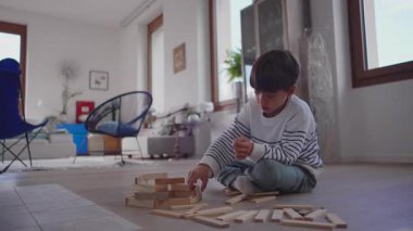 Bir çocuk, ahşap bloklarla oynarken yanına oturması için kardeşini çağırıyor. Nazik iletişim, ortak merak ve çocukluk bağı ile şekillenen sıcak bir kooperatif an yaratıyor.