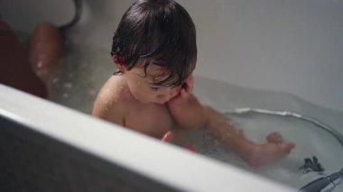 Bir bebek küvette oturuyor, metal duş çubuğunu tutuyor ve suya bakıyor. Sessiz konsantrasyonları, banyo sırasında yapılan ilk keşiflerin doğal ve samimi bir anını yakalar..