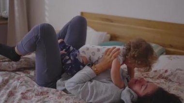 Bir anne ve yeni yürümeye başlayan çocuğu, kaldırdıkları, eğildikleri, sarıldıkları ve birlikte güldükleri, doğal bir bağ, rahatlık ve aile sevgisinin sıcak bir ifadesi olan yatakta neşeli bir sabah anlarını paylaşıyorlar.