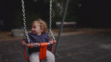 Koltuk ileri geri hareket ederken bir bebek salıncak çubuğuna sıkıca tutunur, hareketle eğilir ve heyecanla gülümser. Sahne kaygısız enerjiyi ve basit çocukluk neşesini yakalar..