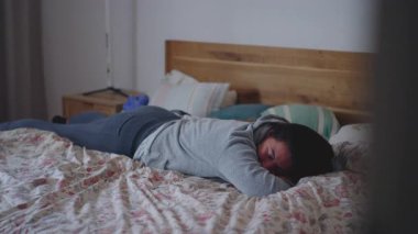 Anne, gözleri yumusak bir sehpaya yaslanmis bir sekilde uzaniyor. Bu arada kucağında yeni yürümeye baslayan, ona dogru uzanan, samimi hareketler, kıkırdamalar ve rahat yatak odasinda aile içi samimiyeti yaratan biri.