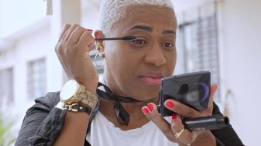 Bir kadın, kişisel makyaj sırasında küçük aynanın önüne göz kapağı ve kasıtlı bakışlarla maskaralık yapıyor.