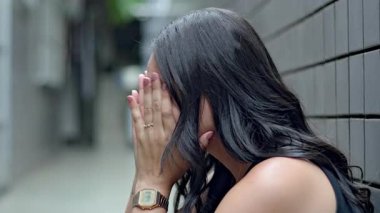 Duvara yaslanmış, elleri yüzü kaplanmış bir kadın yalnızlık anında çaresizlik ve duygusal stres gösteriyor.