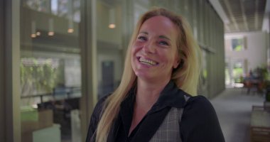 Modern ofis koridorlarında neşe ve açıklıkla gülen bir kadın samimi bir anda pozitif enerji ve otantik duygular yayıyor.