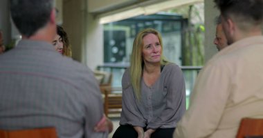Grup terapisi tartışmasına katılan bir kadın, destek çemberindeki akranlarıyla iletişim kurarken duygusal hassasiyet gösteriyor.