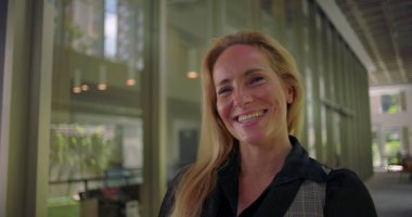 Modern koridorda neşeli bir şekilde gülen kadın, gerçek mutluluğu ve açık ifadeyi gösteriyor, pozitif işyeri duygusunu ve insan bağlantısını temsil ediyor.