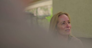 Grup terapisi sırasında duygularıyla konuşan bir kadın derin üzüntü ve hassasiyetini dile getirirken aynı zamanda iyileştirici uzayda destekleyici akranlarıyla iletişim kuruyor.