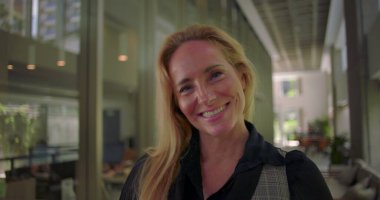 Modern koridorda neşeli bir şekilde gülen kadın, gerçek mutluluğu ve açık ifadeyi gösteriyor, pozitif işyeri duygusunu ve insan bağlantısını temsil ediyor.