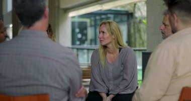 Grup terapisi tartışmasına katılan bir kadın, destek çemberindeki akranlarıyla iletişim kurarken duygusal hassasiyet gösteriyor.