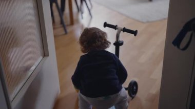 Yürüyen çocuk kaskını çıkarır, scooter 'ı ileri iter, tökezler ve yerde durur, erken denge gelişimini, hassas hassasiyetini, kararlılığını ve sıcak bir aile evinde merakını ifade eder.