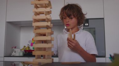 Çocuk uzun ve karmaşık bir kuleye yeni bloklar yerleştiriyor. Sabırlı bir hassasiyetle. Parçaları dikkatlice yerleştiriyor.