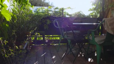 Ahşap güverte balkonu veranda oturma düzeninin etrafındaki yoğun yeşilliklerle dolu. Yavaş anlar, sohbet ve rahat ev hayatı için özel bahçe inzivası havası yaratıyor.