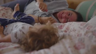 Anne, bebeğin yatağında yatarken sıcak bir şekilde gülümser. Şefkat, duygusal bağ ve huzurlu aile evinde paylaşılan huzur dolu bir varlığın işaretlediği hassas bir anı yakalar.