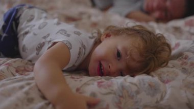 Bebek yatağında yatarken anne arkada dinleniyor. Huzurlu bir sabah rutini içinde güvenlik, sakinlik ve sıcak bağlılığı yansıtan nazik bir aile anı yaratıyor.