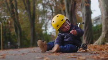 Küçük bir çocuk küçük bir dalı incelemek için yerde durur, sonra süzülerek uzaklaşan scooter 'a doğru döner, bir sonbahar ortamında hassas bir merak, ilgi ve erken öğrenme anı yaratır.