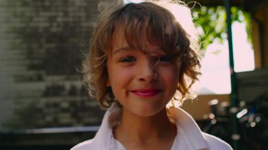 Ardında parlak güneş parıldarken, çocuğun yüzünde yumuşak bir gülümseme belirir, onu sıcak ve parlak bir ışığa sarar ve o ana kolay bir neşe katar.