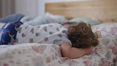 Bebek yatakta uyanıyor, annesine doğru yönelmeden önce battaniyeler üzerinde uyukluyor ve yumuşak, tuhaf bir sabah etkileşimi paylaşıyor. O an, evdeki sessiz sıcaklığı ve sabahın erken saatlerindeki şefkati yakalar..