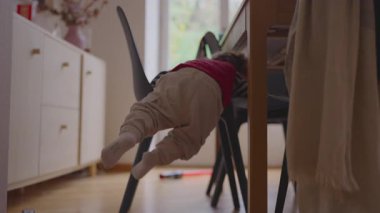 Genç çocuk yardım almadan yemek sandalyesine tırmanıyor, merakını dile getiriyor motor geliştirme özgüveni ve günlük ev ortamını keşfetme dürtüsü