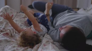 Anne, bebeğini yatakta birlikte yatarken öper. Huzurlu bir aile evinde dinlenme, sıcaklık ve uykusuzluktan uyanma dönemini yansıtan hassas bir bağ kurma anı yaratır.