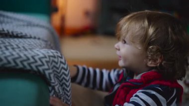 Genç çocuk kanepenin yanında durup, çevreyi dikkatle izliyor, evde sessiz bir zamanda duyarlılık, merak ve güvenlik hissi uyandırıyor.