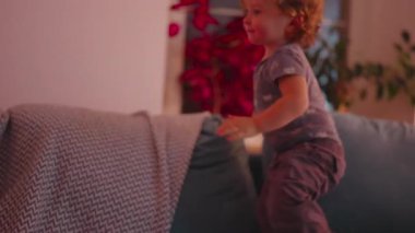 Daha büyük olan çocuk ve bebek kanepede karşı karşıya oturur ve oyun zamanı boyunca, desenli yastıklar ve ev içi mobilyalar ile etkileşime geçerler.