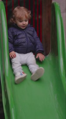 Küçük çocuk sakince hareket geliştirme vücut kontrolünü ve park ortamında bağımsız keşifleri ifade eden yeşil slayttan iniyor