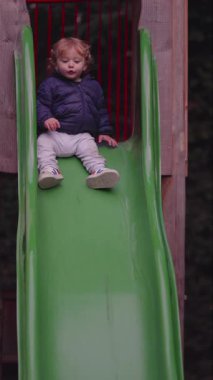 Küçük çocuk, koordineli hareket vücut farkındalığını ve park ortamında erken fiziksel öğrenimi gösteren slaytlarda sorunsuzca aşağı doğru hareket eder