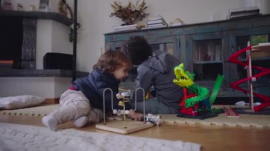 Küçük çocuk yaşam alanında ilk adımlarını atarken, kardeş oynamaya devam ediyor, bağımsızlık, büyüme, keşif ve sıradan aile ritimlerini içeride gösteriyor.