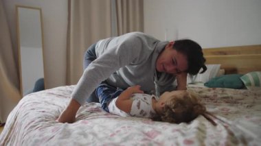 Anne ve çocuk yatakta neşeli bir oyun paylaşıyor, sıcaklığı, yakınlığı, güvenliği, duygusal bağı ve kapalı alandaki otantik aile hayatını ifade ediyorlar.