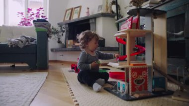 Küçük çocuk otururken oyuncak yapısıyla meşgul olur. Odaklanmış keşifleri ve sakin oyun saatlerini ifade eder.