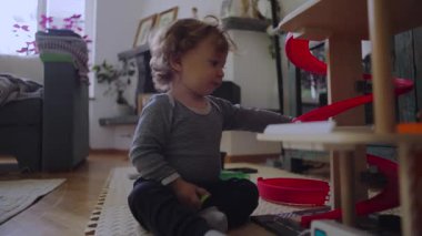 Küçük çocuk, elindeki nesneleri incelerken dikkat çekmeyi, motor keşiflerini ve kapalı alanda sakin oyun saatlerini ifade ediyor.