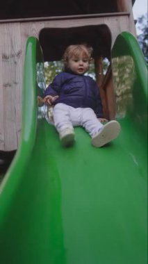 Küçük çocuk, günlük oyun sahasında koordinasyon güveni ve basit keyfi ifade ederek kayarak iniyor