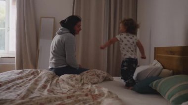Küçük bir çocuğun yatakta özgürce zıplayıp, tırmanıp, oynadığı neşeli bir yatak odası sahnesi. Bu sırada anne gülümsüyor ve nazikçe yol gösteriyor.