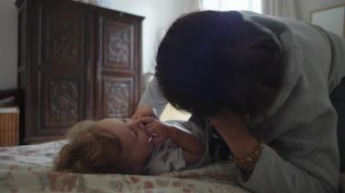 Anne, küçük bebekle yatakta yakın sevgi dolu bir anı paylaşıyor, rahatlık, güven, duygusal güven ve günlük aile hayatında rahat ebeveynlik bağlarını ifade ediyor.