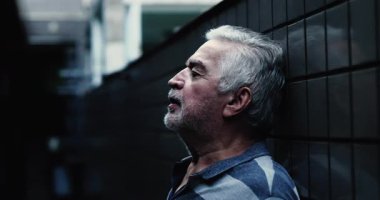 Yaşlı adam seramik duvara karşı durgunluk içinde duruyor, yorgunluğunu, iç düşüncelerini ifade ediyor, ve zor zamanlarda devam etmeye kararlı.