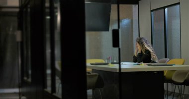Genç bir kadın cam duvarlı ofiste tek başına oturuyor. Yüzü ellere gömülü. Yüksek basınçlı iş gününün ardından bitkin ve duygusal olarak tükenmiş.