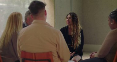 Genç bir kadın grup terapi seansında gözyaşlarıyla derin bir acı ifade ediyor. Güvenli ve şefkatli bir ortamda destekleyici akranlar tarafından çevrelenmiş.