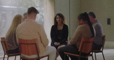 Grup terapisinde konuşan genç bir kadın şefkatli grup üyelerinden oluşan bir çemberde otururken kişisel öyküsünü savunmasızlıkla paylaşıyor.