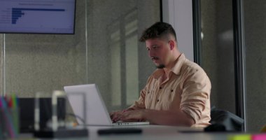 Modern ofis masasındaki dizüstü bilgisayara odaklanmış genç erkek çalışanlar.