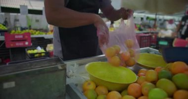 İspanyol sokak satıcısı taze narenciye torbası dağıtıyor. Rutin işlem işlemleri ve mahalle piyasa hayatı içindeki anlamlı bağlantıları aktarıyor.